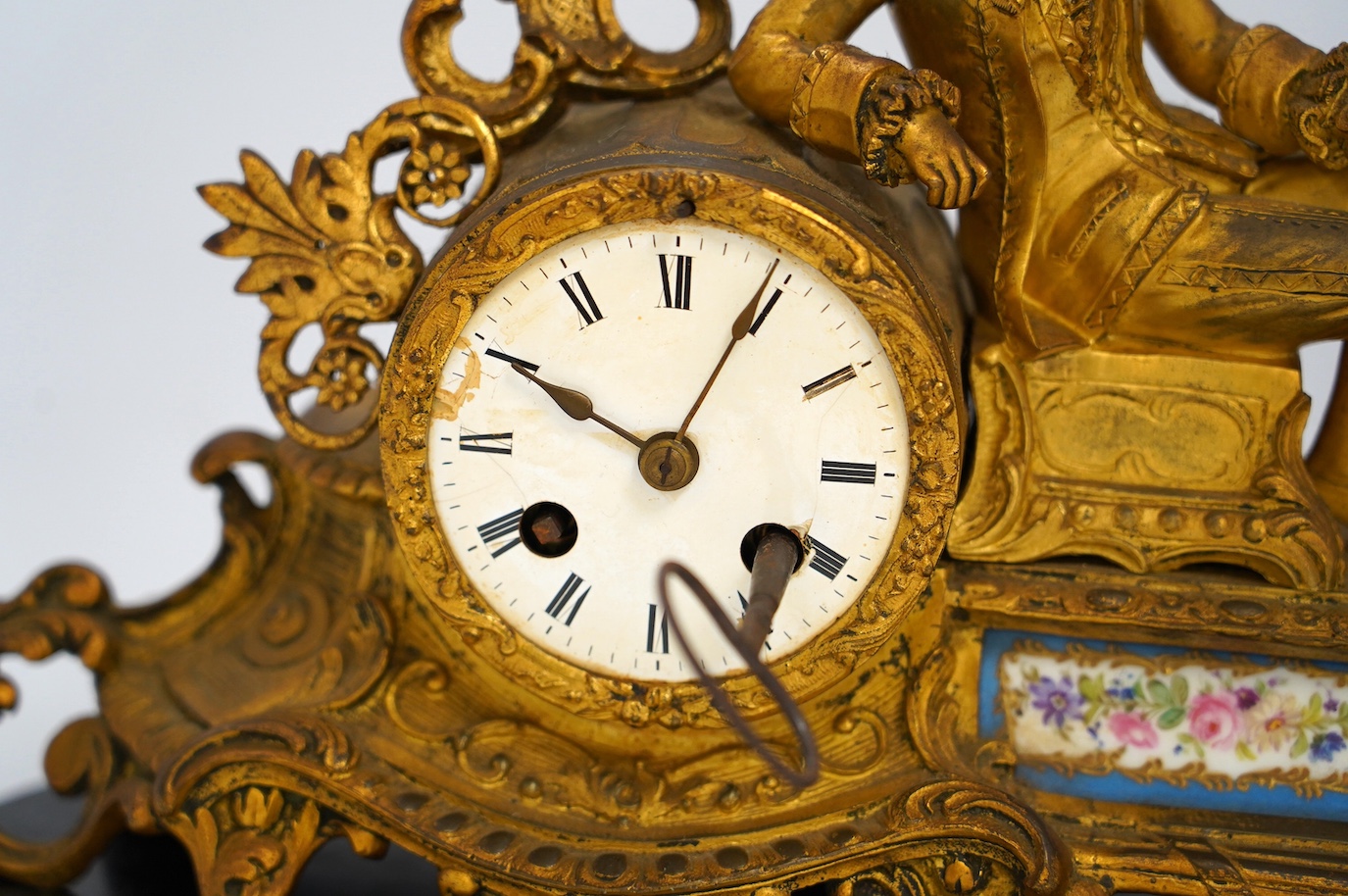 A 19th century figurative ormolu mantel clock, with floral porcelain panels, on stand with key and pendulum, stand approximately 39cm wide. Condition - clock dial cracked, clock untested as working